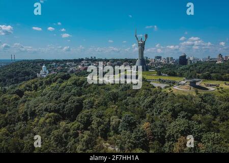 Panorama di Motherland monumento a Kiev pappando fuori della foresta in una giornata di sole con cielo blu. Maestosa foto di una grande statua sulla collina di Kvyv, U. Foto Stock