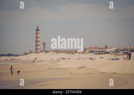 Spiaggia di sabbia Praia da barra in portogallo in una giornata di sole con un grande faro rosso e bianco sullo sfondo. Foto Stock