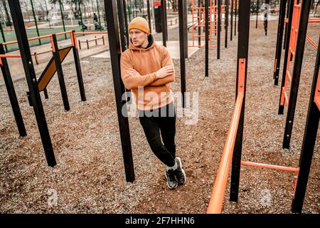 Giovane uomo in outfit sportivo facendo allenamento mattutino all'aperto. Giovane uomo che riposa su un terreno sportivo di strada. Mantenersi in forma e concetto sano Foto Stock