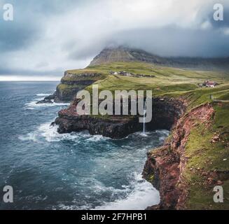 Vista aerea del drone del villaggio di Gasadalur e Mulafossur la sua cascata iconica, Vagar, Isole Faroe, Danimarca. Vista approssimativa nell'oceano atlantico settentrionale. Lussureggiante Foto Stock