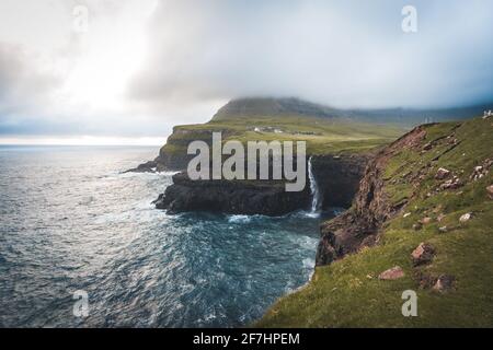 Vista aerea del drone del villaggio di Gasadalur e Mulafossur la sua cascata iconica, Vagar, Isole Faroe, Danimarca. Vista approssimativa nell'oceano atlantico settentrionale. Lussureggiante Foto Stock