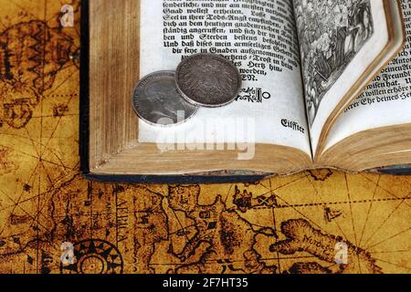 Vecchie monete d'argento del 1902 e un libro antico da 1763 su una mappa del mondo Foto Stock