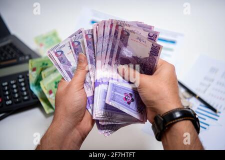 Mani degli uomini che tengono e contando le banconote della Banca Qatari. 500 nuove note di Rial. Concetto di business e finanza Foto Stock