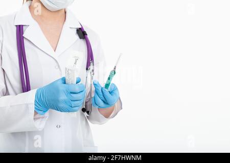 Un giovane infermiere in una maschera apre una siringa su sfondo bianco in un cappotto bianco, per fare una vaccinazione, un'iniezione. Il concetto di vaccinazione e. Foto Stock