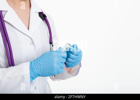 Un giovane infermiere in una maschera apre una siringa su sfondo bianco in un cappotto bianco, per fare una vaccinazione, un'iniezione. Il concetto di vaccinazione e. Foto Stock