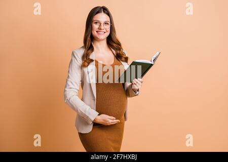 Foto di affascinante dolce signora che aspetta il bambino vestito marrone tummy lettura sfondo di colore beige isolato Foto Stock