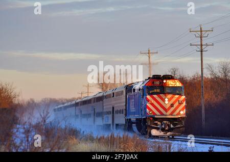Bartlett, Illinois, Stati Uniti. Un treno per pendolari Metra disturba la neve durante il viaggio fino alla luce finale del giorno. Foto Stock