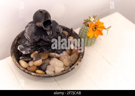 zen acqua fondente su uno sfondo bianco accanto a un fiore arancione in un piccolo vaso. Foto Stock
