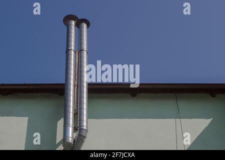 Due tubi di ventilazione alimentano e scaricano aria e gas dalla caldaia a gas all'ultimo piano della casa sopra il tetto su sfondo blu cielo. Concetto: Preparazione Foto Stock