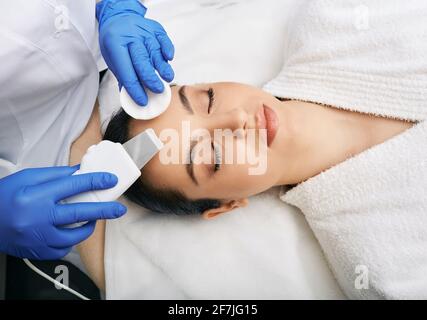 Peeling viso ecografico. Donna di brunette che ottiene pelle ultrasonica di buccia con scrubber della pelle alla clinica di cosmetologia Foto Stock