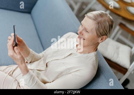 bella signora si sta rilassando sul divano utilizzando le app sul suo smartphone. Foto Stock