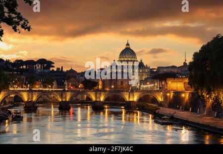 Roma Italia. Basilica di San Pietro in Vaticano sopra il ponte illuminato Sant'Angelo e il fiume Tevere vista notturna, cielo di colore arancio dopo il tramonto Foto Stock