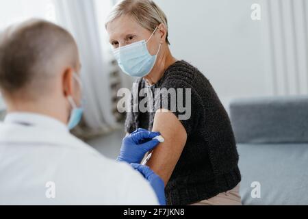 medico in guanti protettivi vaccinando una donna matura. Foto Stock