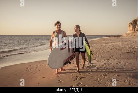 Coppia matura con tavole da surf sulla bellissima spiaggia godendo di paradiso e di uno stile di vita attivo. Bella forma uomo e donna surf e divertirsi. In trave Foto Stock