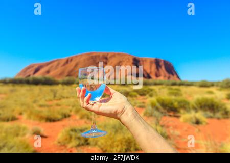 Donna di mano che regge un calice di vetro riflettente che Ayers Rock in Uluru-Kata Tjuta National Park, Australia centrale, Northern Territory. Toast in Foto Stock