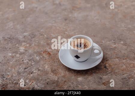 Tazza di caffè su sfondo grigio, una tazza di caffè con crema e gocce di cioccolato su uno splendido sfondo grigio con striature arancioni Foto Stock