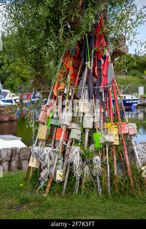 Pali e bandiere per marcare trappole di pesce si appoggiano contro un albero nel porticciolo di Zempin sull'isola di Usedom. Foto Stock