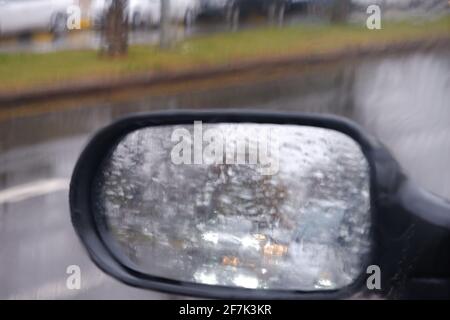 Vista dallo specchio retrovisore in una giornata piovosa con acqua gocce Foto Stock