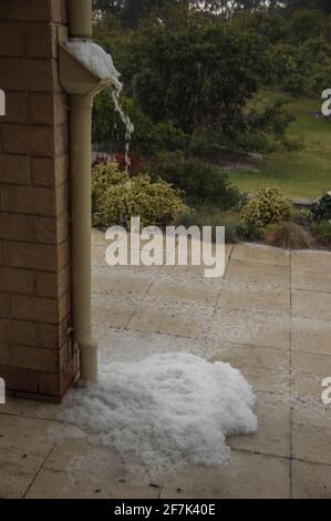 Pietre di grandine che scorrono giù il tubo dell'acqua, raccogliendo sulla rete del filtro e sul terreno durante la tempesta di tuono. Giardino privato, Queensland, Australia. Foto Stock