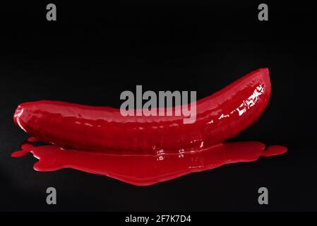 Primo piano e ancora vita di una banana pelata, che è stata adustata con vernice rossa, su uno sfondo scuro Foto Stock