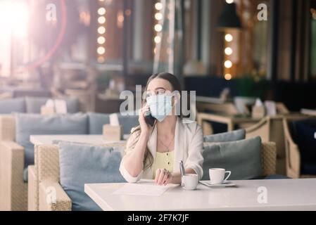 La manager femminile in tuta e maschera medica lavora a distanza in via caffè. Foto Stock