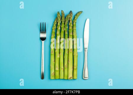 Asparagi con forchetta e coltello su fondo blu. Asparagi vegetali freschi per una dieta e una nutrizione sana. Verdure e concetto di cibo sano. Foto di alta qualità Foto Stock