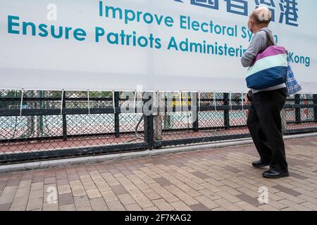 Hong Kong, Cina. 8 aprile 2021. Un uomo guarda un cartello del governo appeso su una recinzione da parco giochi che recita "migliorare il sistema elettorale garantire i patrioti che amministrano Hong Kong". (Foto di Miguel candela/SOPA Images/Sipa USA) Credit: Sipa USA/Alamy Live News Foto Stock