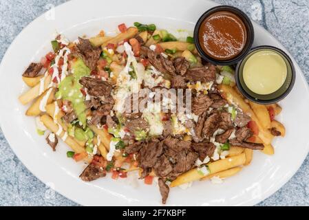 Vista dall'alto del grande piatto di patatine fritte Asada ricoperte di formaggio servito con salsa di immersione tenterà tutti. Foto Stock