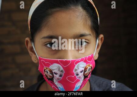 Bambina indiana o asiatica che indossa la maschera facciale come protezione personale contro l'inquinamento atmosferico o coronavirus COVID-19. Giovane hipster in maschera protettiva Foto Stock