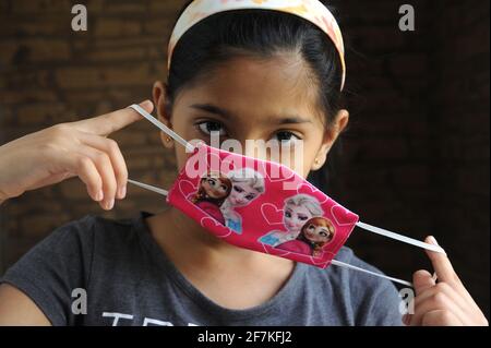 Bambina indiana o asiatica che indossa la maschera facciale come protezione personale contro l'inquinamento atmosferico o coronavirus COVID-19. Giovane hipster in maschera protettiva Foto Stock