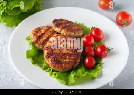 Cotoletta fritta con insalata e pomodori in un piatto bianco su sfondo grigio Foto Stock