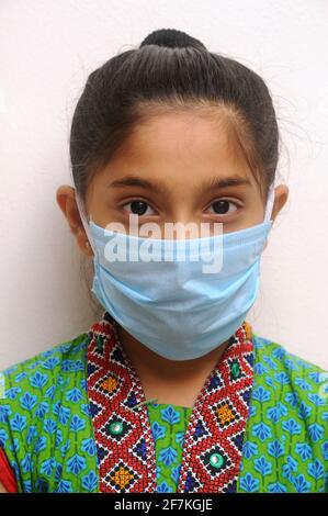 Bambina indiana o asiatica che indossa la maschera facciale come protezione personale contro l'inquinamento atmosferico o coronavirus COVID-19. Giovane hipster in maschera protettiva Foto Stock