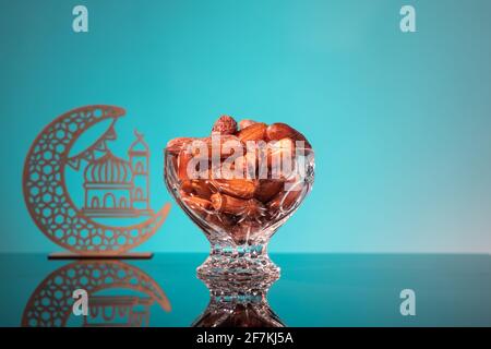 Iftar musulmano di rottura del digiuno durante il mese di Ramadan con date dolci conservate. Mezzaluna decorativa e moschea sullo sfondo come prop Foto Stock