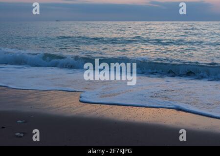 Serata di sabbia marina. Ora blu dopo il tramonto sul mare. Gli ultimi raggi del sole si riflettono nelle onde. Scivola di schiuma di mare sulla spiaggia. T Foto Stock