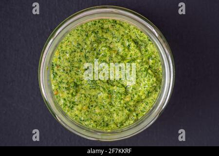 Salsa di pesto verde in un recipiente di vetro isolato su sfondo nero, primo piano, vista dall'alto. Salsa di pesto fresco fatta con aglio selvatico, pinoli, sale e pepe Foto Stock