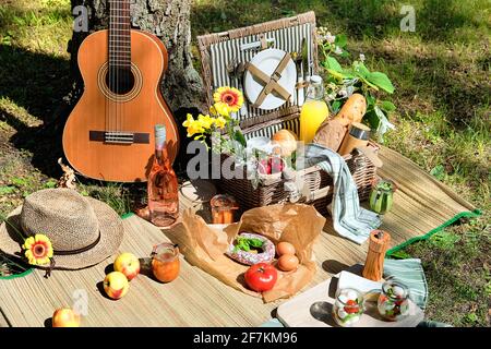 Cestino da picnic d'epoca, cesto con baguette e limonata all'aperto su un'erba con formaggio, mozzarella, pomodori, ciliegie, vite. Chitarra, spuntini Foto Stock