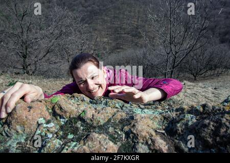 Arrampicata femminile su roccia verso il bordo superiore della scogliera. Vista dall'alto delle mani della donna appese sul bordo. Concetto di forza. Foto Stock