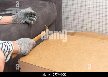 Le mani degli uomini, indossando guanti, tenere un martello e martellare un chiodo. Costruzione di mobili per la casa, librerie per un ufficio domestico. Foto Stock