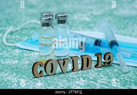 Prevenzione delle malattie stagionali. Fiale mediche, siringhe e una maschera su sfondo verde. Vaccinazione contro covid-19. Foto Stock