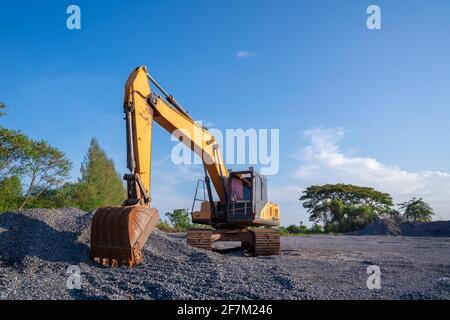 Escavatore cingolato parcheggiato su terreno in pietra su sfondo blu in cantiere Foto Stock