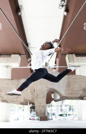 Ballerino africano americano che esegue un salto acrobatico in città all'aperto. Concetto di danza urbana. Spazio per il testo. Foto Stock