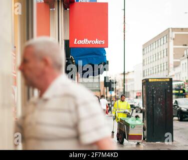 Giocatore irriconoscibile, uomo di mezza età che cammina in un negozio di scommesse Ladbrokes. Scommesse sportive, gioco d'azzardo stile di vita. Camden High St, Londra, Regno Unito. Ago 2015 Foto Stock