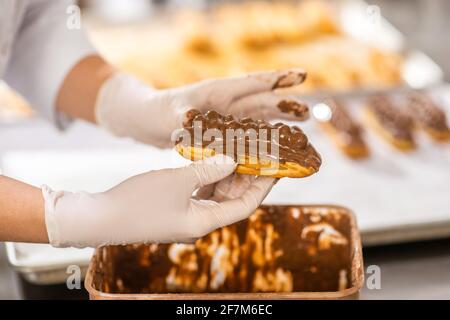 I pasticceri mani tengono il eclair nella guarnizione di cioccolato Foto Stock