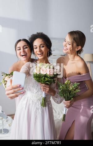 sposa afroamericana che prende selfie con bridesmaids allegri a casa Foto Stock