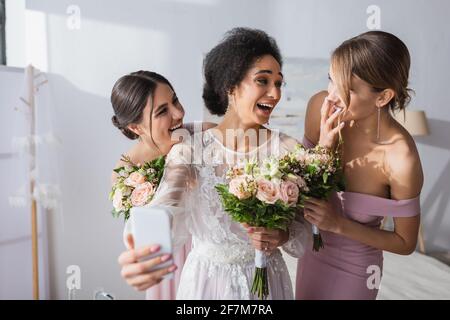 ridendo sposa afroamericana prendendo selfie con amici allegri, in primo piano offuscato Foto Stock