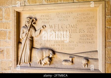 Cartello di benvenuto multilingue scolpito in pietra nel portico della chiesa di St Edwards nella città di Cotswold di Stow on the Wold, Gloucestershire UK Foto Stock