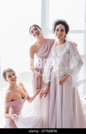 gioiosa sposa afroamericana sorridente a macchina fotografica vicino bridesmaids felice Foto Stock