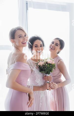 bride afroamericana entusiasta guardando la macchina fotografica vicino bridesmaids felice Foto Stock