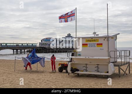 I bagnini RNLI si preparano per la stagione che ci attende a Bournemouth Beach, Bournemouth, Dorset UK in aprile - erigendo gazebo - rispettare l'acqua Foto Stock