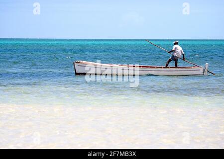 Uomo locale spingendo la sua tradizionale barca di legno nel colorato Oceano Indiano, Rodrigues Island, Mauritius Foto Stock